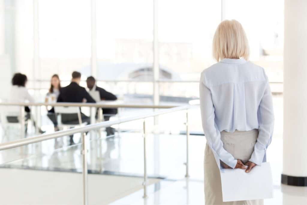 Stock image of older woman being excluded at work.