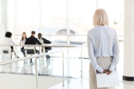 Stock image of older woman being excluded at work.