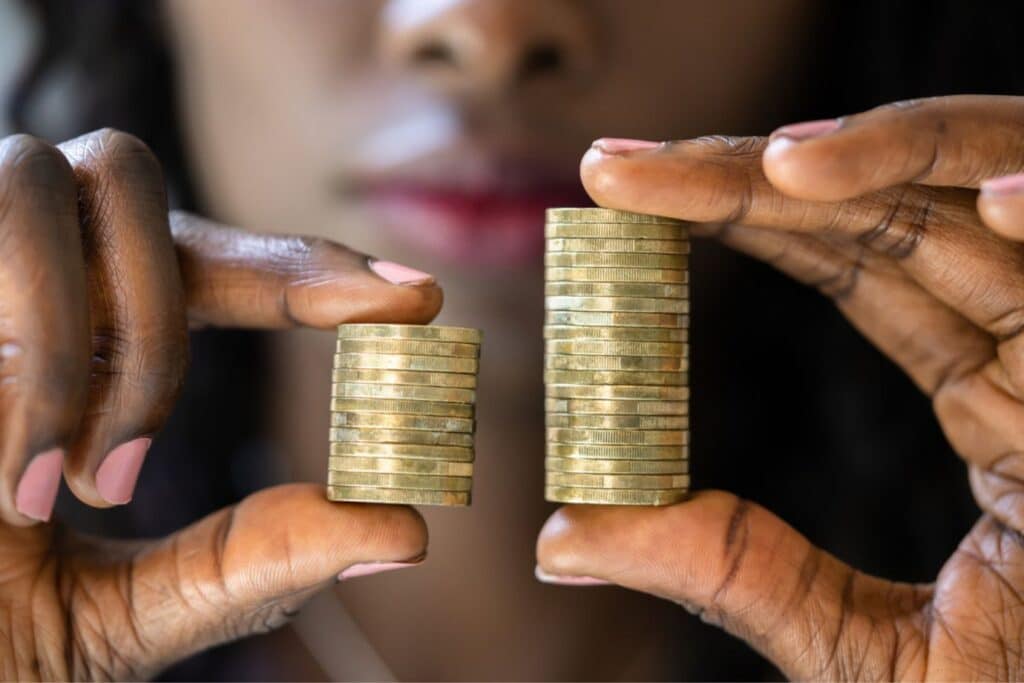 Stock image: Woman holding uneven piles of gold coins, representing the international gender pay gap.