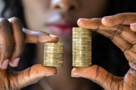 Stock image: Woman holding uneven piles of gold coins, representing the international gender pay gap.