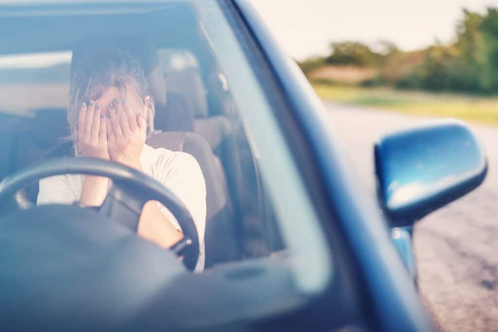 Woman sitting in car head in hands, upset