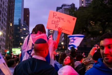 Woman dressed in Israeli flag holding sign that reads "rape is not resistence"