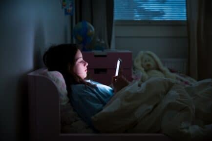 girl lying in bed scrolling on smart phone