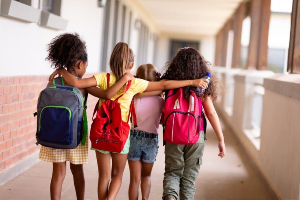 Rear shot of four girls walking with their arms around each other at school