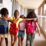 Rear shot of four girls walking with their arms around each other at school