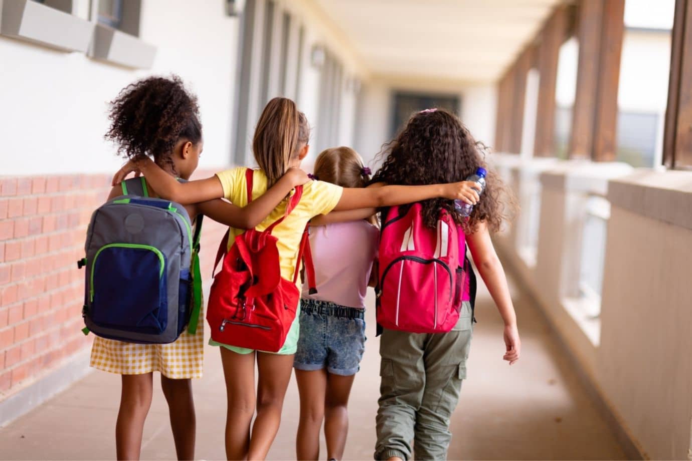 Rear shot of four girls walking with their arms around each other at school