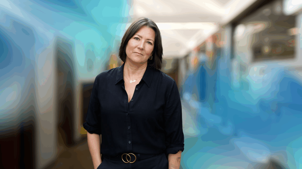 CEO of Project F, Emma Jones, standing in an office hallway, looking straight into camera and wearing a black shirt and black trousers.