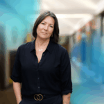 CEO of Project F, Emma Jones, standing in an office hallway, looking straight into camera and wearing a black shirt and black trousers.