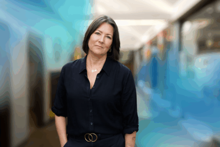 CEO of Project F, Emma Jones, standing in an office hallway, looking straight into camera and wearing a black shirt and black trousers.